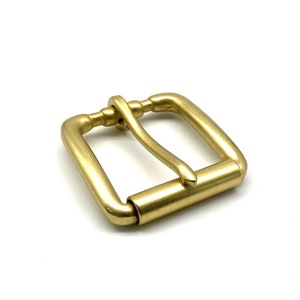 May include: A solid brass buckle with a smooth, polished finish. The buckle is designed for a 1-inch strap and has a simple, rectangular shape.