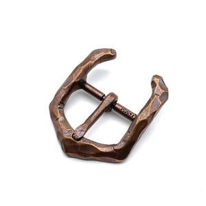 Peut inclure: Boucle de ceinture en métal de couleur bronze et de forme rectangulaire. La boucle présente un aspect martelé et une barre centrale pour la sangle. Le texte "36MM" est visible sur la barre. Conçue pour une sangle.