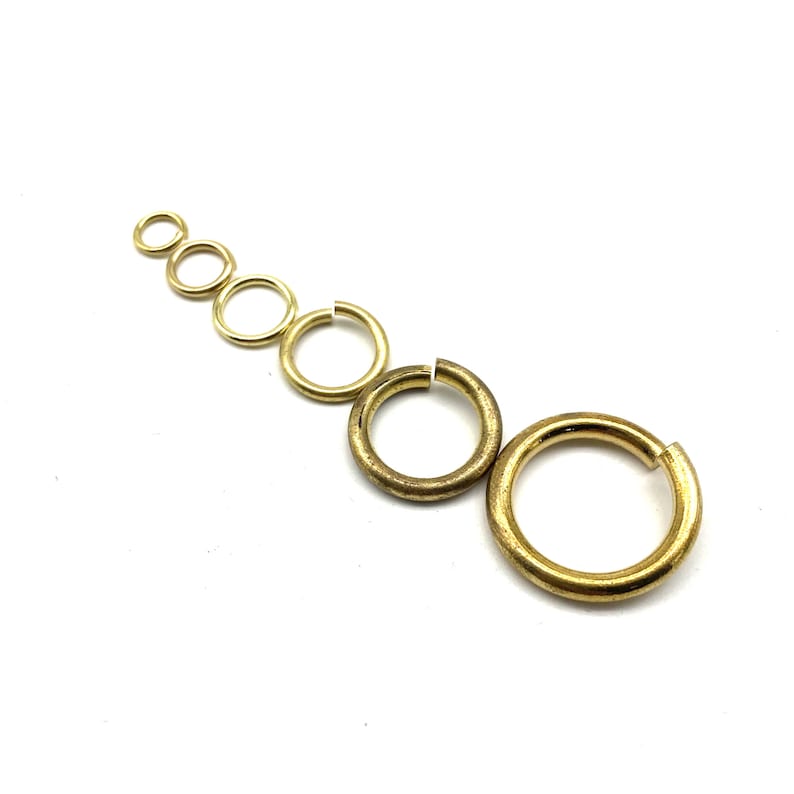 May include: A set of seven gold jump rings of varying sizes. The rings are arranged in a diagonal line from largest to smallest.