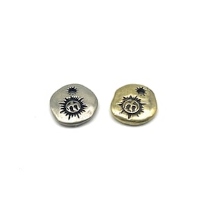 Peut inclure: Deux breloques rondes en métal avec un motif soleil et étoile. Une breloque est argentée et l'autre est dorée.