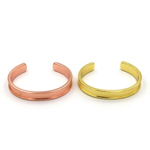 Könnte beinhalten: Zwei schlichte Armreifen, einer in Roségold und einer in Gold. Beide Armreifen haben ein flaches, breites Band.