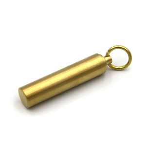 May include: A small, gold-colored metal container with a screw-on lid and a key ring attached. The container is about 2 inches long and is perfect for holding small items like pills or a key.