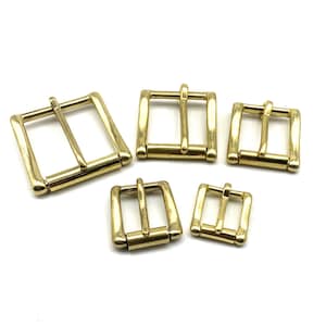 May include: Five gold-toned metal belt buckles of varying sizes. The buckles are all rectangular in shape with a single, centered, horizontal bar.