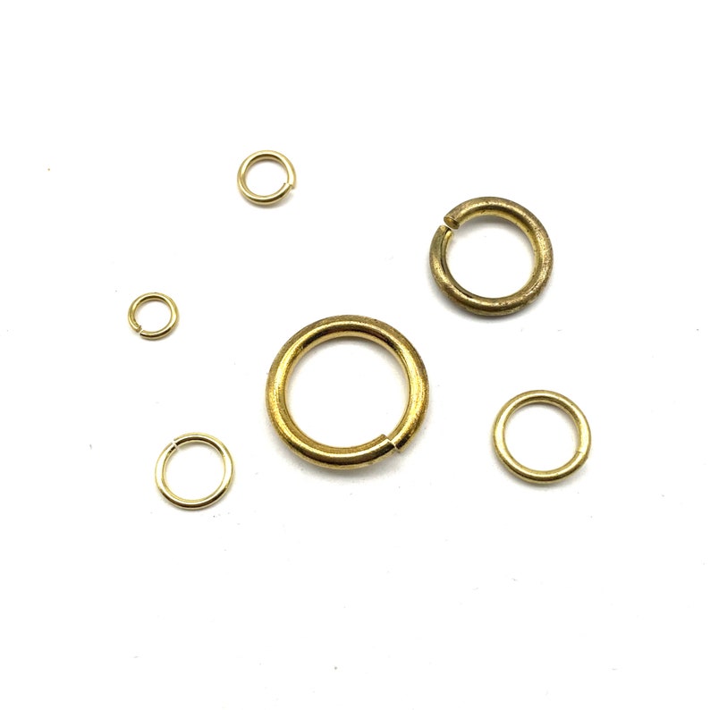 May include: Assortment of five gold jump rings of varying sizes. The jump rings are made of metal and are used for jewelry making.