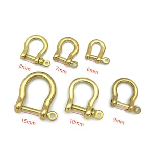 Könnte beinhalten: Ein Satz von sechs goldfarbenen D-Ringen aus Metall in verschiedenen Größen von 6 mm bis 15 mm. Die Ringe sind in einer Reihe angeordnet, wobei der kleinste Ring links und der größte Ring rechts liegt. Jeder Ring hat einen Schraubverschluss.