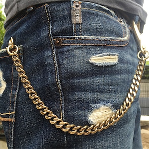 May include: A gold chain wallet chain hanging from the front pocket of a pair of blue jeans. The jeans have a distressed look with rips and tears.