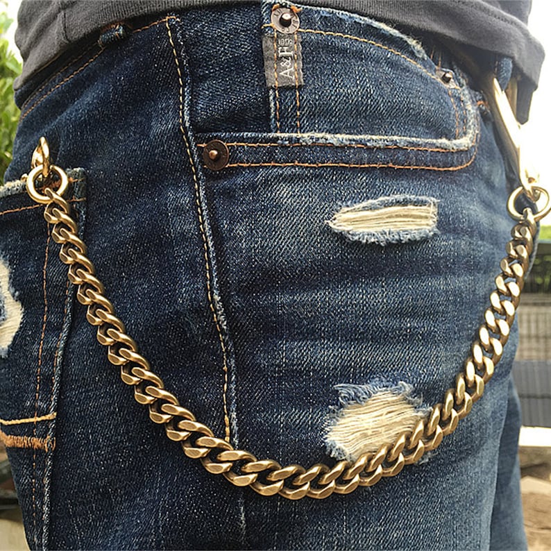 May include: A gold chain wallet chain hanging from the front pocket of a pair of blue jeans. The jeans have a distressed look with rips and tears.
