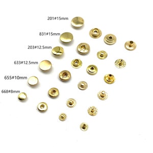 Puede incluir: Surtido de botones a presión de metal dorado en varios tamaños, incluyendo 8 mm, 10 mm, 12,5 mm y 15 mm. Los botones a presión están dispuestos sobre un fondo blanco.