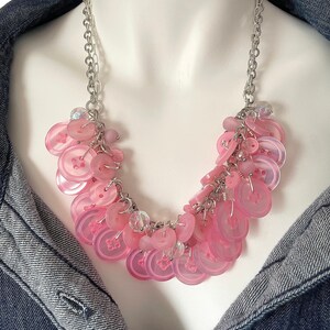 May include: A pink button necklace with a silver chain. The buttons are arranged in a cascading pattern and are accented with clear crystals.