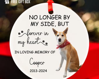 May include: A white ceramic ornament with a red ribbon for hanging. The ornament features a photo of a dog wearing a red bandana. Text reads "NO LONGER BY MY SIDE, BUT forever in my heart. In loving memory of Cooper 2013-2024."