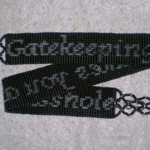 May include: Black beaded necklace with a silver clasp. The beads are arranged in a pattern that spells out "Gotcha" and "Don't you dare" in silver beads.