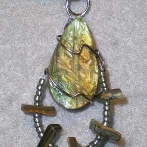 May include: A handcrafted pendant necklace featuring a pear-shaped, iridescent green and gold shell. The shell is wrapped in silver wire and accented with a beaded, curved design with small, rectangular, brown-green beads. The necklace has a black cord.