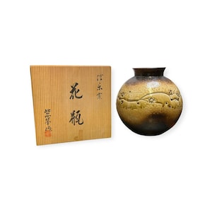 Peut inclure: Un vase en céramique avec une finition dégradée marron et or, orné d'un motif floral. Le vase est accompagné d'une boîte en bois avec des caractères japonais. Le vase a une forme ronde avec un col étroit.