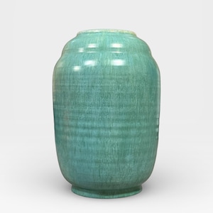 Op de afbeelding: Een turquoise keramische vaas met een afgeronde body en een licht uitlopende rand. De vaas heeft een getextureerd oppervlak en een subtiel, horizontaal geribbeld patroon. De basis is een donkerdere tint turquoise.