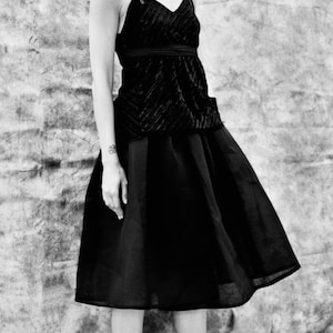 Puede incluir: Un top de terciopelo negro con una falda negra. El top tiene cuello en V y tirantes finos. La falda es de línea A y llega a las rodillas.