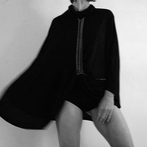 May include: A black cape with a long chain necklace. The cape is worn by a person with their legs and feet visible.