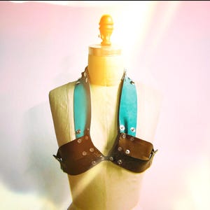 Puede incluir: Un top halter de cuero negro con tirantes turquesa y tachuelas plateadas. El top está en un maniquí.