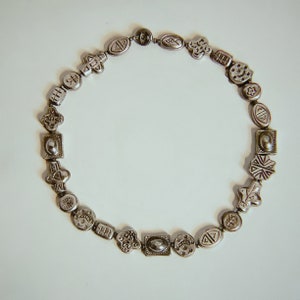 May include: A silver necklace with a variety of charms, including geometric shapes, symbols, and small figures. The necklace is made of metal and has a silver finish.