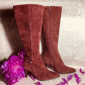 May include: A pair of burgundy suede knee-high boots with a stiletto heel and a back zipper closure.