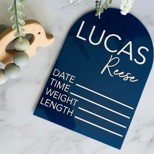 May include: A dark blue acrylic sign with rounded top edges and white text. The sign says "Lucas Reese" and has lines for "Date", "Time", "Weight", and "Length".
