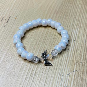 May include: White beaded bracelet with a silver angel wing charm. The beads are iridescent and have a subtle shimmer.