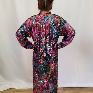 May include: A long, sequined dress with a floral pattern in shades of pink, blue, green, and gold. The dress has long sleeves and a loose fit.