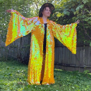 May include: A long, yellow sequined kimono with iridescent detailing. The kimono has wide sleeves and a flowing silhouette.