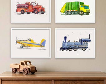 Op de afbeelding: Vier ingelijste aquareldrukken met een rode brandweerwagen, een groene en gele vuilniswagen, een geel en blauw vliegtuig en een blauwe stoomlocomotief. Onder de prenten staat een kleine speelgoedvrachtwagen van naturel hout op een houten dressoir.