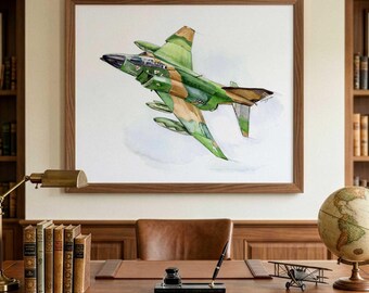 May include: A framed watercolor painting of a military jet aircraft in flight, featuring a camouflage pattern of green, brown, and tan colors. The jet is depicted at an upward angle against a white background, displayed in a wooden frame.
