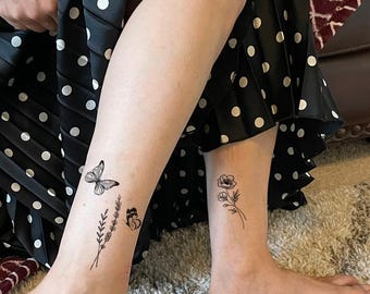 May include: Temporary tattoos featuring black ink designs applied to the lower legs. One leg displays a butterfly and a sprig of lavender, while the other leg features a small floral stem with two blossoms, all rendered in a fine line art style.