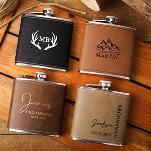 Pode incluir: Quatro frascos de quadril personalizados em couro preto, castanho e bege. Cada frasco tem uma tampa prateada e é gravado com texto e desenhos personalizados, incluindo iniciais, nomes e datas. Os frascos estão dispostos sobre uma superfície de madeira.