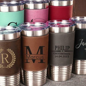 Puede incluir: Conjunto de ocho vasos de acero inoxidable personalizados con envolturas de imitaci&oacute;n de cuero. Cada vaso presenta un nombre y un dise&ntilde;o diferentes, incluidas iniciales, una corona y las palabras "Groomsmen" y "Jacob".
