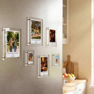 Könnte beinhalten: Eine Sammlung klarer magnetischer Acryl-Fotorahmen in verschiedenen Größen, die an einer Edelstahl-Kühlschranktür befestigt sind. Jeder Rahmen enthält ein Foto mit dem Text "the beautiful moments of life". Die Fotos zeigen Menschen.