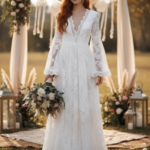 May include: A white lace wedding dress with a plunging neckline and long, flared sleeves. The dress features intricate floral lace detailing and a flowing skirt. The bride is holding a bouquet of white and green flowers. The setting is outdoors with a decorative arch.