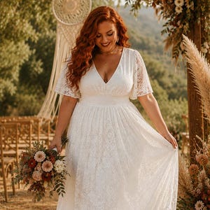 May include: A white lace dress with a V-neckline, flutter sleeves, and a cinched waist. The dress features an all-over floral lace pattern with a flowing skirt. The garment is held by a person carrying a bouquet of dried flowers in shades of rust, cream, and brown.