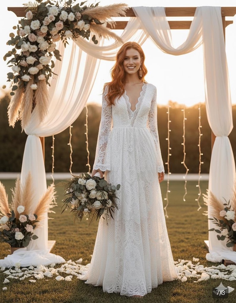 May include: A white lace wedding dress with long sleeves and a deep V-neck. The bride is holding a bouquet of white and green flowers. The ceremony backdrop includes a wooden arch, white draping fabric, and floral arrangements.