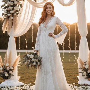 May include: A white lace wedding dress with long sleeves and a plunging neckline. The bride is holding a bouquet of white flowers. The ceremony is outdoors, with a floral arch and string lights in the background.