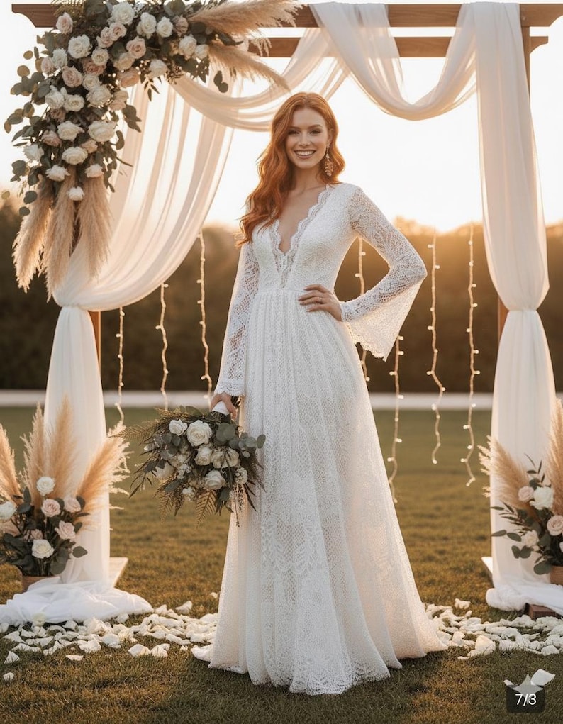 May include: A white lace wedding dress with long sleeves and a plunging neckline. The bride is holding a bouquet of white flowers. The ceremony is outdoors, with a floral arch and string lights in the background.