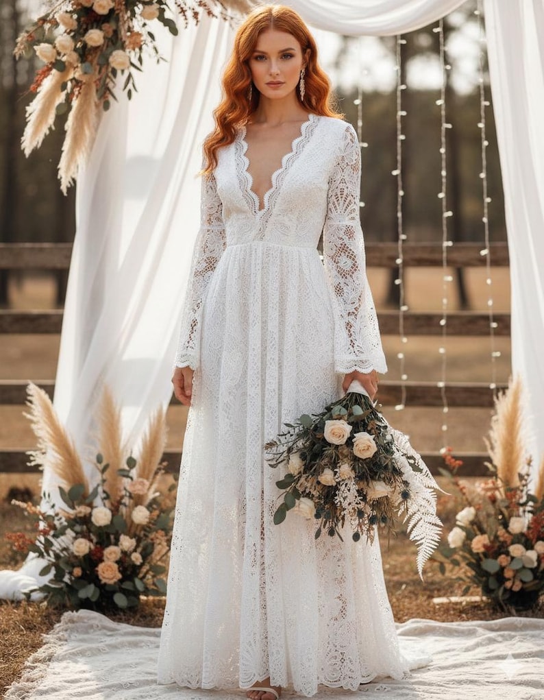 May include: A white lace wedding dress with a plunging neckline and long sleeves. The dress features a flowing A-line skirt and is held by a person. The person is holding a bouquet of white and green flowers. The dress is suitable for a wedding.