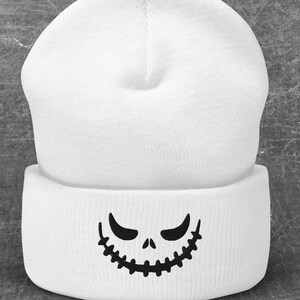 May include: White beanie with a black Jack Skellington-style face on the front. The beanie is on a gray background with black bats and spiders.