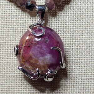 May include: A pink gemstone pendant with a silver wire design, hanging from a beaded necklace.