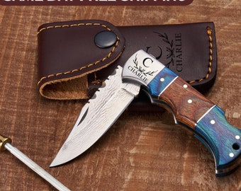 May include: A personalized pocket knife with a blue and brown wooden handle. The blade is partially open and has a serrated edge. The knife is engraved with the letter "C" and the name "Charlie". It comes with a brown leather sheath.