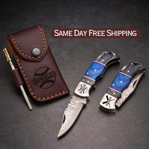 May include: Two personalized pocket knives with blue and black wood handles. One knife has a baseball graphic and the name "WHEELER" engraved on it. The other knife has a baseball bat graphic and the name "FREEMAN" engraved on it. The knives come with a brown leather sheath.