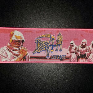 May include: Pink rectangular patch featuring the word "DEATH" in a stylized font with a scythe and a figure. The word "LEPROSY" is below. The patch has an illustration of a robed figure and three robed figures. The patch has a pink border.