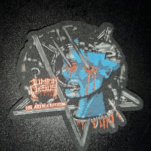 May include: A black and white embroidered patch with a blue and red image of a person's head with the text "Limpin' Jesus" and "The Art of Crucifying" below the image.