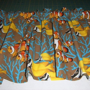 May include: A brown fabric valance with a repeating pattern of orange and white clownfish swimming among blue coral branches and yellow seaweed.