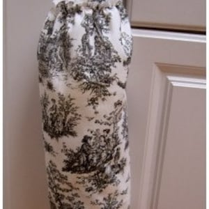 May include: A white fabric bag with a black and white toile pattern. The bag has a drawstring closure and a loop at the top for hanging. The bag is hanging on a white cabinet door.