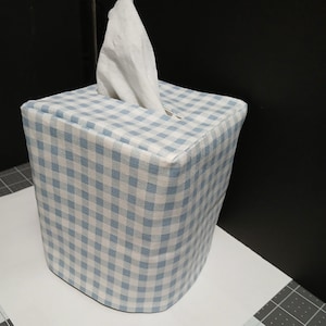 May include: A blue and white gingham tissue box cover. The cover is square and has a small opening on the top for tissues to be pulled out.
