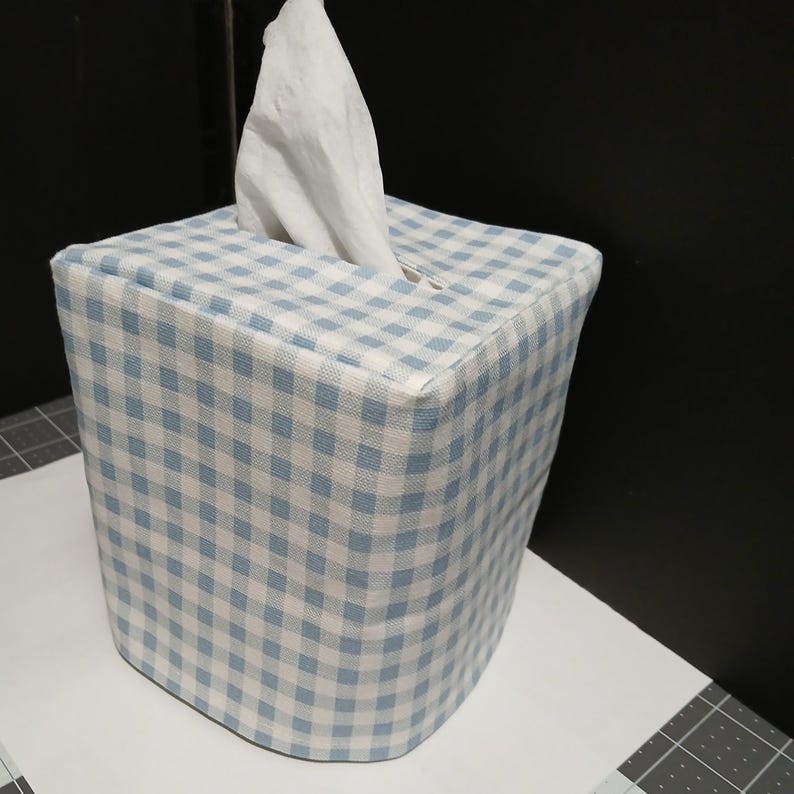 May include: A blue and white gingham tissue box cover. The cover is square and has a small opening on the top for tissues to be pulled out.