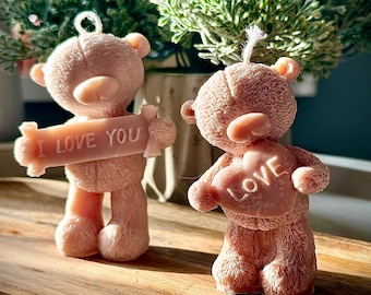 Pode incluir: Duas velas de urso de peluche rosa, uma segurando um cartaz que diz "Eu te amo" e a outra segurando um coração que diz "Amor".